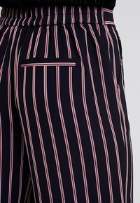 Pantalones a rayas marineros con rayas verticales en rojo y blanco, cinturilla elástica y un pequeño bolsillo trasero con un ribete en contraste.