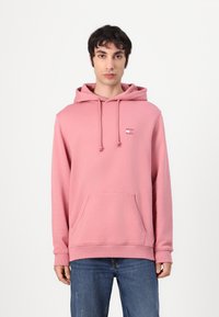 Felpa rosa con cappuccio e cordini, tasca a marsupio, polsini e orlo a coste. Texture morbida e dettaglio logo minimalista sul petto.