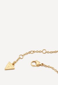 Bracciale a catena con finitura dorata caratterizzato da un charm triangolare inciso con la scritta "GUESS" e chiusura a moschettone. Design a maglie con finitura lucida.