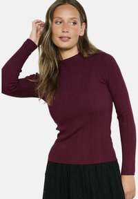 Burgundijas krāsas ribota garām piedurknēm augšdaļa ar augstu apkakli, izgatavota no teksturēta adījuma auduma. Saskaņota ar melnu, mežģīņu tekstūras svārku.