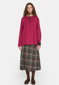 Fioletowa bluzka z długim rękawem i kapturem, w połączeniu z kraciastą spódnicą w odcieniach szarości, zieleni i burgundu. Brązowe buty i dopasowana chustka.