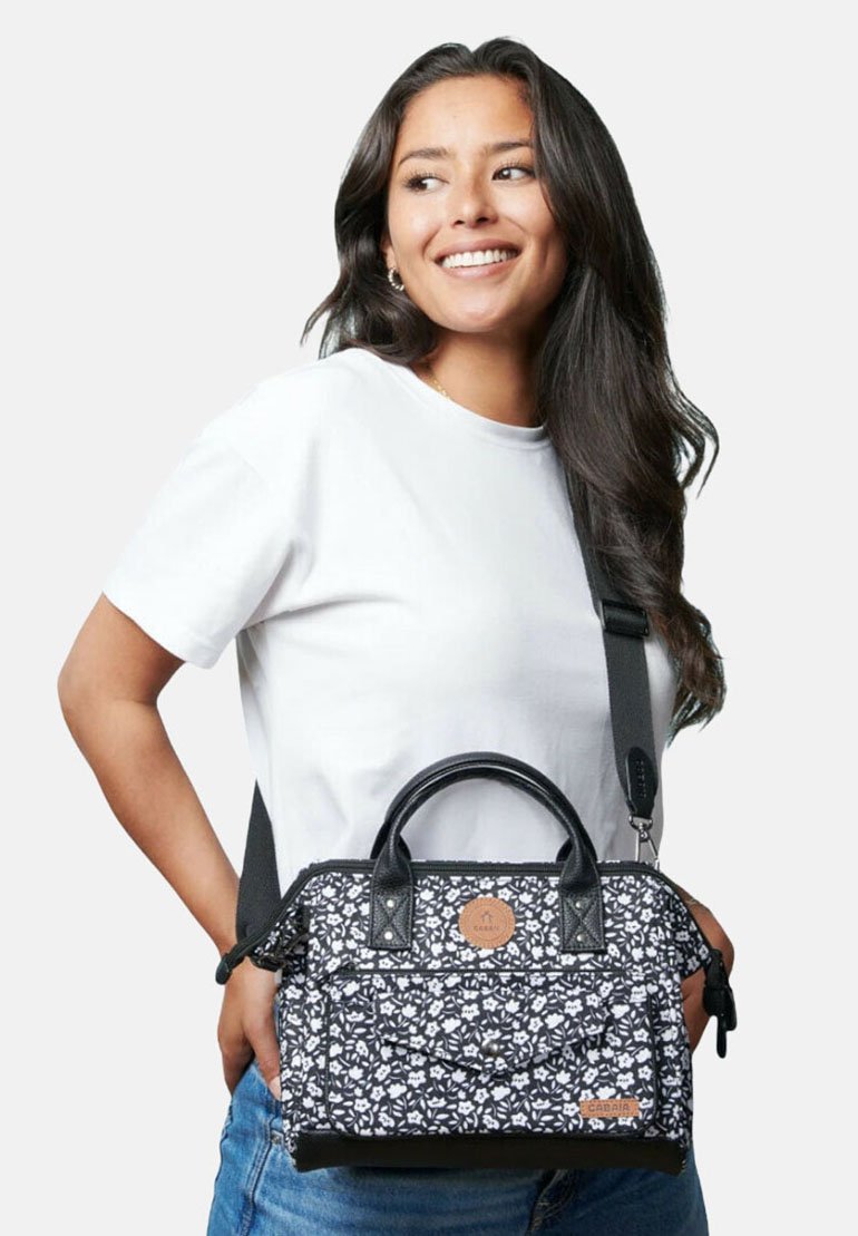 Black floral-patterned handbag with a structured shape, leather-like accents, dual top handles, and an adjustable shoulder strap.