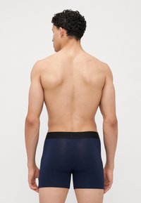 Dunkelblaue Boxershorts mit einem schwarzen elastischen Bund, die eine enge Passform und eine glatte Textur aufweisen, aus der Rückansicht präsentiert.