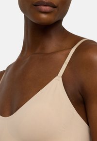 Ljusbeige sömlös bh med justerbara remmar, slät yta och triangulär koppform. Minimalistisk design, ingen synlig hårdvara.