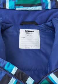 Niebieska kurtka wodoodporna od wewnątrz z wielokolorowymi wzorami geometrycznymi, metka z instrukcjami pielęgnacji oraz miękka tekstura.