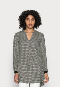 Blusa de manga longa em padrão preto e branco com decote em V. Apresenta punhos ligeiramente ajustados e um corte solto e fluido, com a parte de trás mais longa.