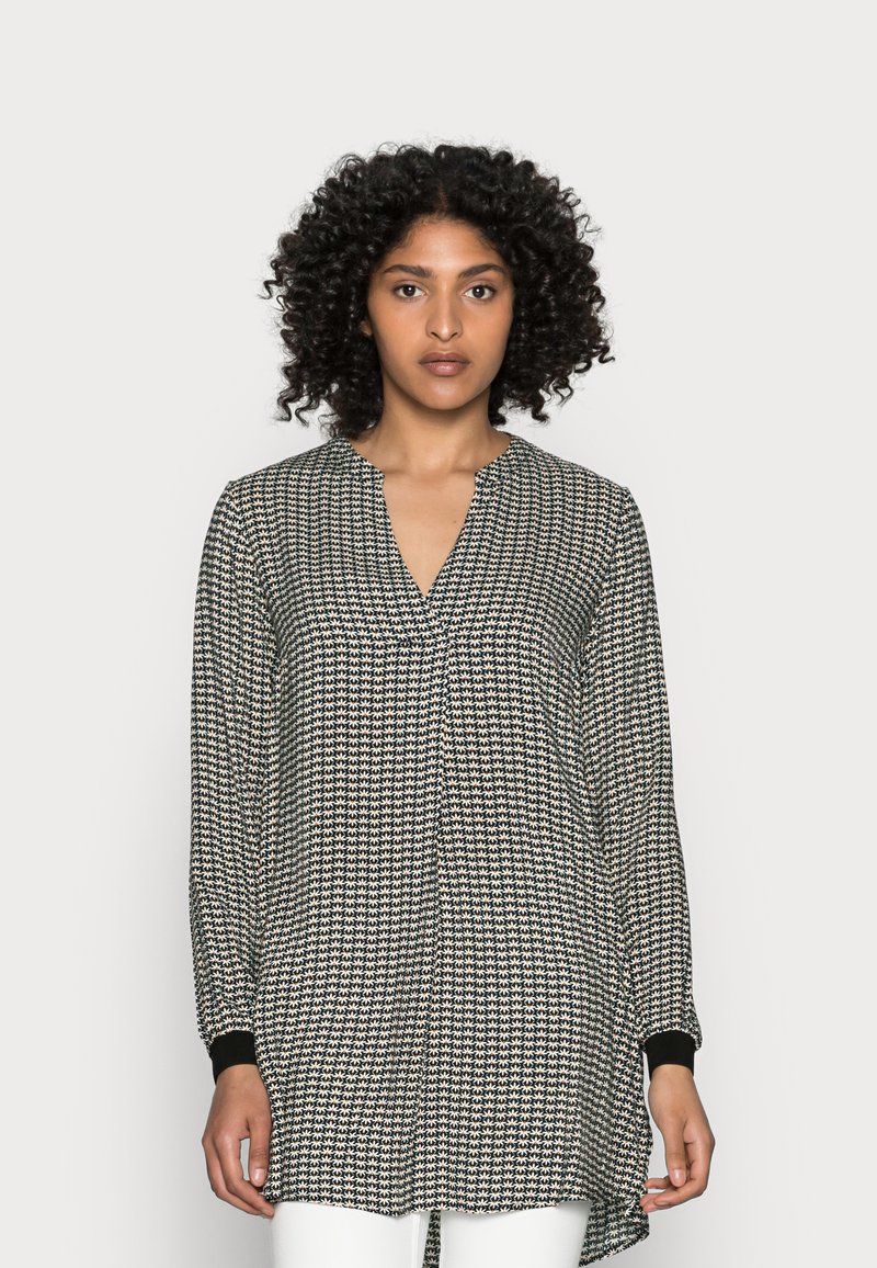 Blusa de manga longa em padrão preto e branco com decote em V. Apresenta punhos ligeiramente ajustados e um corte solto e fluido, com a parte de trás mais longa.