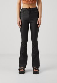 Pantaloni neri a sigaretta a zampa d'elefante realizzati in materiale lucido, con vita media e dettagli delle tasche frontali sottili, abbinati a scarpe con piattaforma chunky.