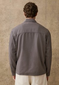 Szara, lekka kurtka z kołnierzem, długimi rękawami i prostym dołem. Charakteryzuje się prostym przeszyciem i gładką fakturą.