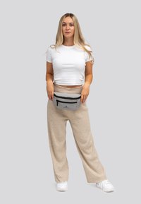Grijze heuptas met zwarte ritsaccenten, brede band en logo, gedragen met beige wijde broek en een strak wit t-shirt.