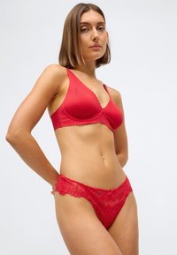 Roter BH mit gewelltem Rand und glatter Textur; passende rote Spitzenunterwäsche mit aufwendigem Muster und transparenten Details.