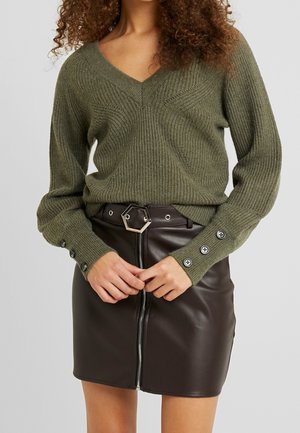 Olive green knitted sweater with a V-neck and textured detailing, paired with a fitted brown faux leather skirt featuring a front zipper and button accents.