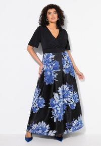 Maxikleid mit schwarzem Oberteil, kurzen Ärmeln und einem blauen Blumenmuster auf dem Satinrock. V-Ausschnitt und blaue hohe Absätze.