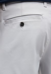 Πίσω τσέπη ανοιχτόχρωμου γκρι παντελονιού με ένα μαύρο κουμπί και λεπτομέρεια με στενή τσέπη, φορεμένο με σκούρα μπλε ζώνη.