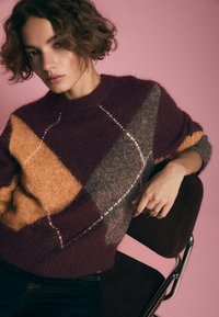 Maglione lavorato a maglia con motivo a rombi in bordeaux, arancione e grigio. Morbido al tatto, colletto rotondo, con cuciture a contrasto.