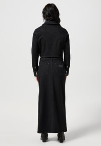 Czarna dżinsowa długa spódnica z dopasowanym pasem, długimi rękawami, detalami na plecach oraz zatrzaskami przy mankietach. Gładka faktura i prosty krój.