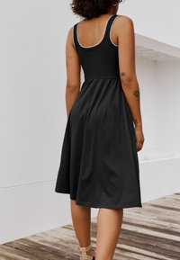 Rochie neagră fără mâneci, cu un corset ajustat și o fustă fluidă, având un tiv contrastant pe decolteu și o textură moale a materialului.