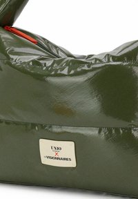 Grüne glänzende Tasche mit glänzendem Finish, ausgestattet mit einem orangefarbenen Reißverschluss und einem Etikett mit der Aufschrift „UNIO X LES VISIONNAIRES“ in einem rechteckigen Rahmen.