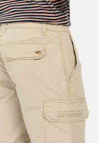 Beige cargo shorts met zijzak, achterzak met borduursel met de tekst "MADE FOR DAILY ADVENTURES", en gestikte details. Katoenen materiaal.