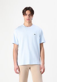 Tricou din bumbac de culoare bleu deschis, cu mâneci scurte, decolteu rotund și un mic logo brodat verde în zona stângă a pieptului.