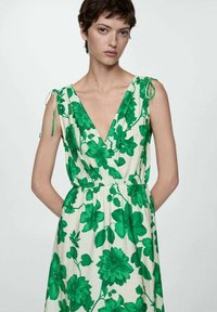 Haljina bez rukava s dubokim V-izrezom, strukirana, zelena cvjetna uzorak na svijetloj pozadini, s detaljima na ramena sa vezicom.