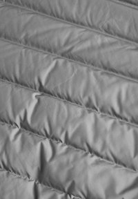 Sivi jastučić tekstil s quilt strukturom, koji sadrži dijagonalne šavove i gladak, blago sjajan površinski sloj.