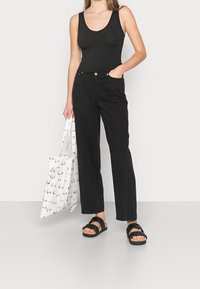 Svart ribbad tanktop matchat med högmidjade svarta byxor. Svarta sandaler med korksula och en vit tote-väska med grafiskt mönster.