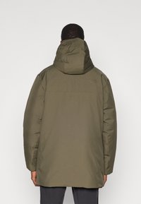 Parka verde oliva con cappuccio, caratterizzata da una texture liscia, maniche lunghe e un taglio dritto. Il retro presenta elementi di design minimali.