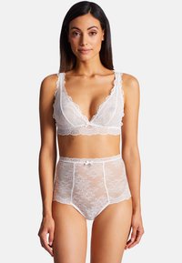 Ensemble de lingerie en dentelle blanche comprenant un bralette aux bords festonnés et une culotte taille haute ornée d'un délicat nœud à la taille.