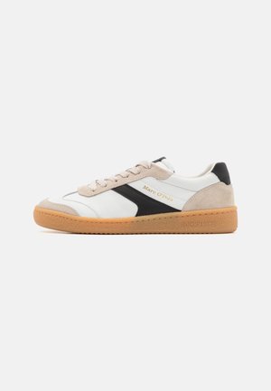 Weiße Sneaker mit schwarzen und beigen Wildlederakzenten, runde Zehenform, Schnürung an der Vorderseite und einer strukturierten Gummisohle. Goldene Logo-Details an der Seite.