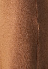 Bruine rekbare stof met een zachte textuur en fijne ribbels. Het materiaal lijkt glad en aansluitend, wat het strakke ontwerp benadrukt.