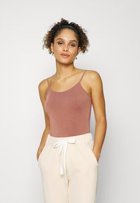 Body na cor rosa envelhecido com alças finas tipo espaguete, combinado com calças creme de cintura elástica com um accentuador de laço branco.