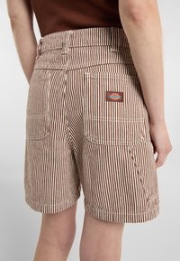 Pantalones cortos a rayas marrones y crema con cintura alta, que cuentan con dos bolsillos traseros y un pequeño parche de logo rectangular en el bolsillo derecho.