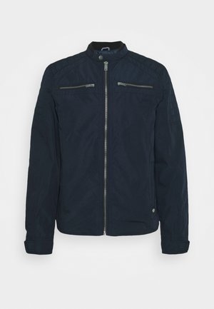 Donkerblauwe herenjas met ritssluiting aan de voorkant, opstaand kraag met drukknoop, twee horizontale borstzakken met rits en lange mouwen.