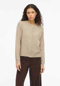 Smėlio spalvos kardiganas, pagamintas iš minkštos megztos medžiagos, su apvalia iškirpte, ilgomis rankovėmis ir perlų imitacijos sagomis priekyje. Vienodo rašto tekstūra.