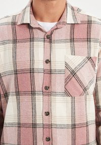 Geruit flanellen overhemd in roze, wit en zwart. Voorzien van een knoopsluiting aan de voorkant, lange mouwen en een borstzak met een bijpassend patroon.