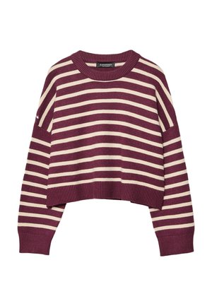 Kobieta ubrana w krótki sweter w poziome bordowe i kremowe paski z długimi rękawami na jednolitym tle.