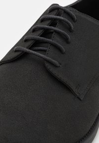 Chaussure à lacets en daim noir avec dessus texturé, lacets plats lisses et languette structurée. Dotée d'une semelle en caoutchouc profilée et basse.