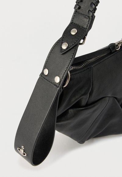 Μαύρη δερμάτινη τσάντα με φαρδιά λουράκι που διαθέτει ασημένιους σταυρωτούς πείρους και ένα μικρό ασημένιο έμβλημα σε σχήμα πλανήτη κοντά στο άκρο του λουριού, φερμουάρ εν μέρει ορατό.