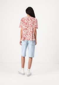 Rød- og hvitblomstret kortermet skjorte, kombinert med lyseblå knelang shorts og hvite høy-top sneakers.
