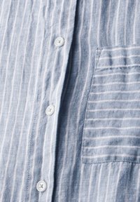 Camicia di lino a righe blu chiaro con righe verticali bianche, taschino sul petto e bottoni bianchi lungo la patta anteriore.