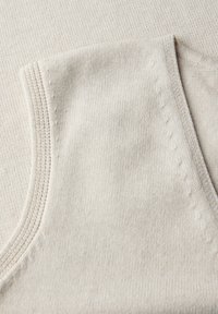 Mjuk beige stickad tyg med ribbad texturdetalj och ett fint stygnmönster längs kanten, vilket antyder ett plagg eller textilartikel.