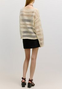Strickpullover in Creme mit horizontalen Streifen, lockerer Passform, weitem Ausschnitt und langen Ärmeln, kombiniert mit einem schwarzen Minirock und klobigen Sandalen.