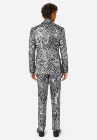 Traje en blanco y negro con un patrón geométrico de estrellas y líneas alternas. El atuendo incluye una chaqueta ajustada y pantalones entallados.