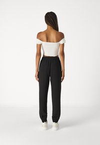 White off-the-shoulder cropped top paired with black elastic-waist tapered pants and white sneakers with accent details.