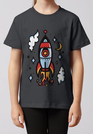 Kind trägt dunkles T-Shirt mit farbenfroher Cartoon-Rakete beim Start, umgeben von Sternen, Wolken und einer Mondsichel.