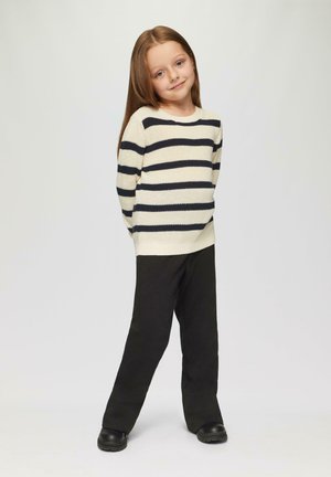 Pull crème avec des rayures navy, col rond, texture tricotée ; associé avec un pantalon noir et des chaussures noires. Pose debout devant un fond neutre.