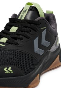 Black athletic shoe featuring mesh fabric, rubber sole, and reflective accents. Includes a lace-lock system and green pull tab for fastening.