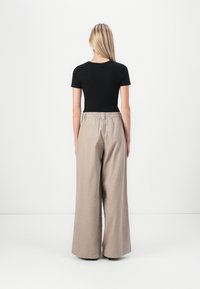 Sort kortærmet top parret med højtaljede, brede beige bukser. Stoffet ser glat ud; bukserne har en elastisk talje og en afslappet pasform.