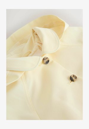 Světlé žluté tričko s překládaným límcem, dvěma černými knoflíky a hladkou texturou s jemným proužkovaným vzorem uvnitř.